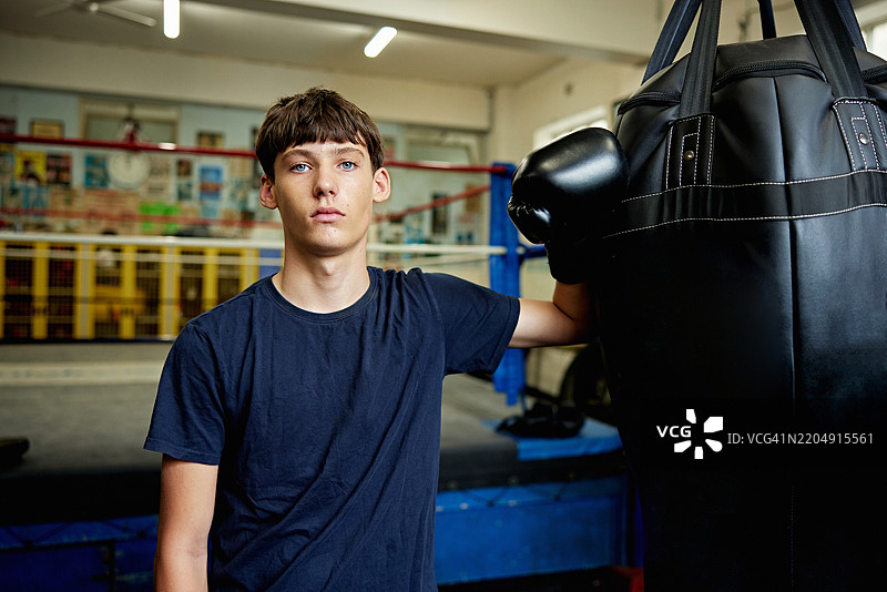 拳击台边的青少年男性拳击手与重沙袋的肖像图片素材