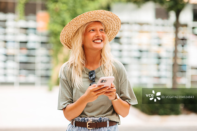 戴着草帽的晒黑金发女孩在发短信图片素材