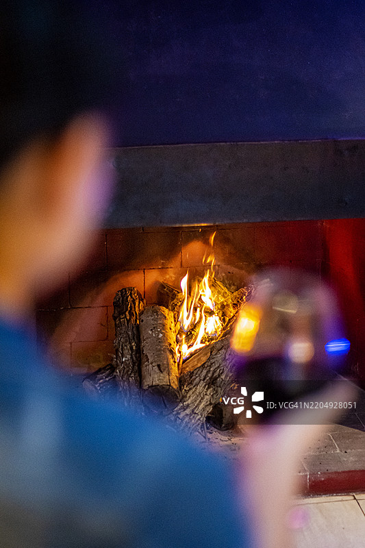 女人手持一杯红酒，身旁有一个点燃的壁炉图片素材