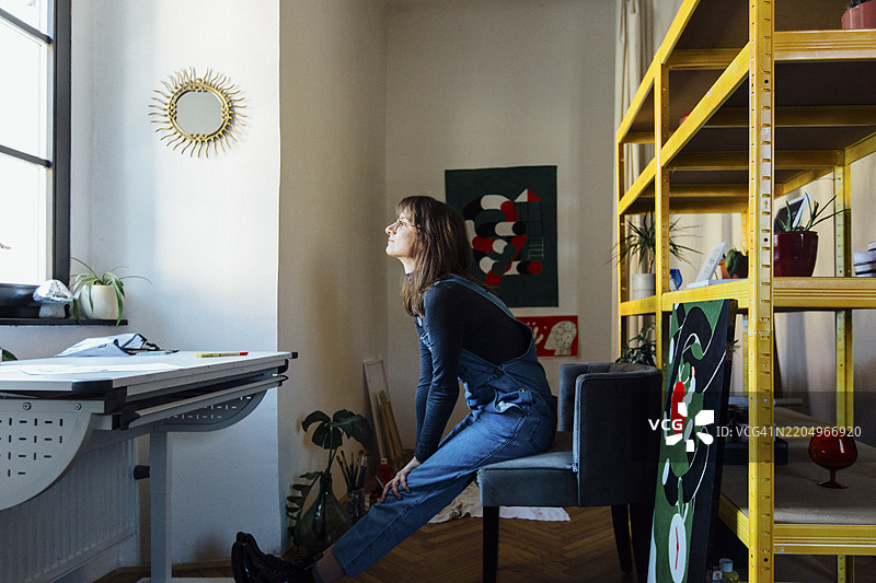 穿着牛仔工装的艺术家在创意工作室的椅子上放松。图片素材