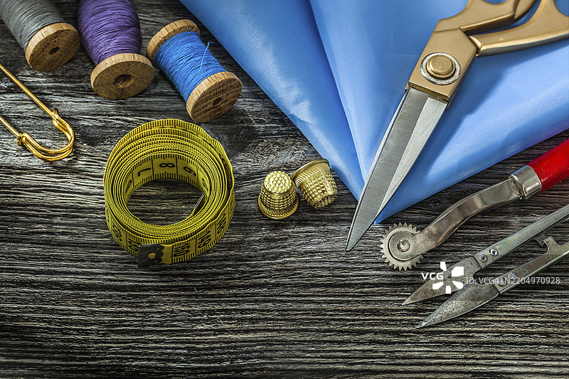 缝纫工具组合：测量带、顶针、线和剪刀放在复古木材上图片素材