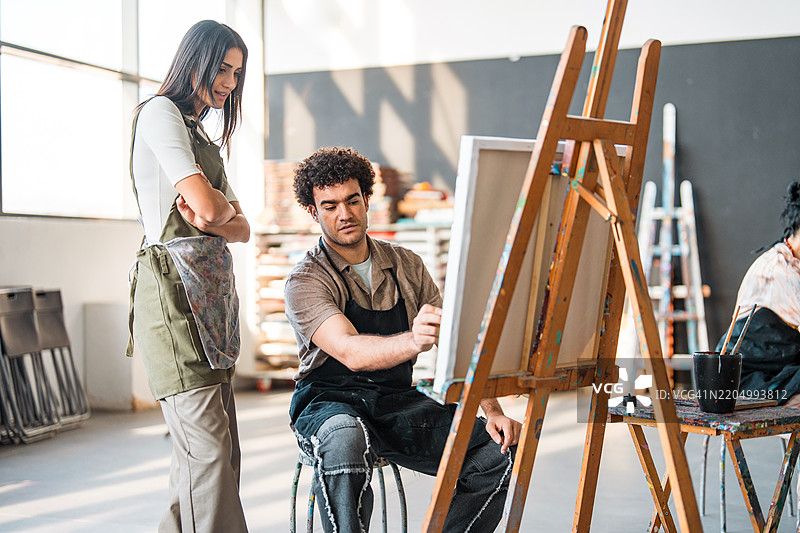 年轻的中东艺术学生在明亮的工作室里接受导师的指导图片素材