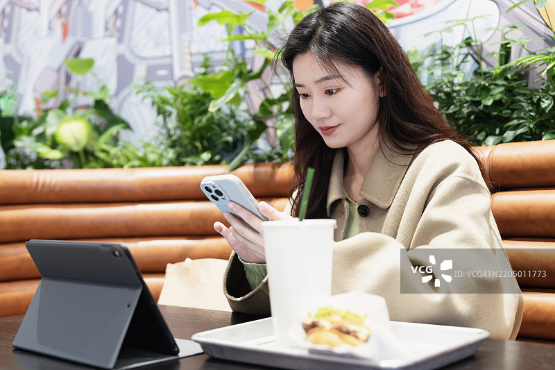 美丽的年轻亚洲女性在餐厅用餐时使用智能手机。图片素材