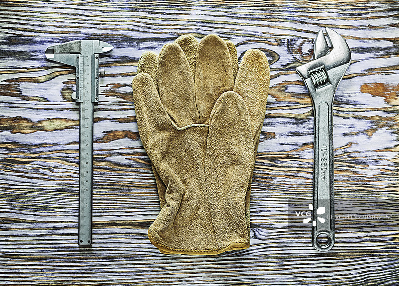 木板上的游标卡尺、可调扳手和安全手套图片素材