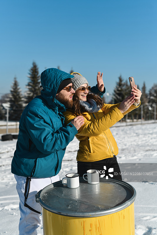 兴奋的情侣在阳光明媚的雪山上视频通话，向亲人挥手致意图片素材
