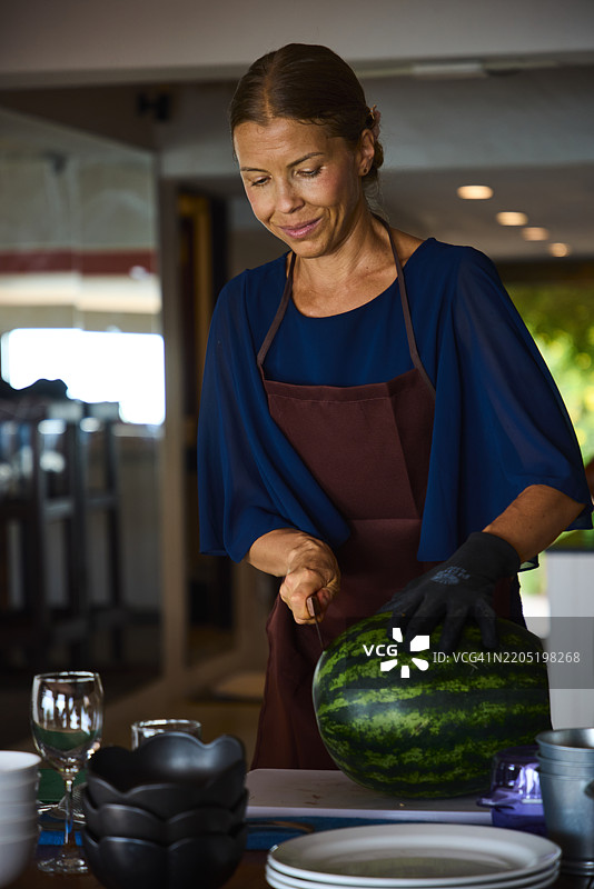 穿着围裙的女人在阳光明媚的室内厨房里切西瓜图片素材