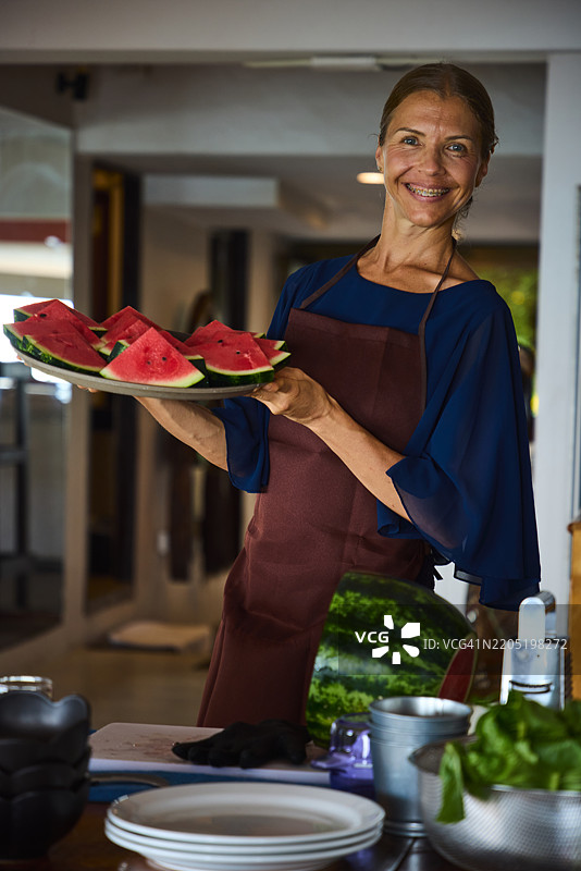 微笑的女性在厨房里端着一盘西瓜片图片素材