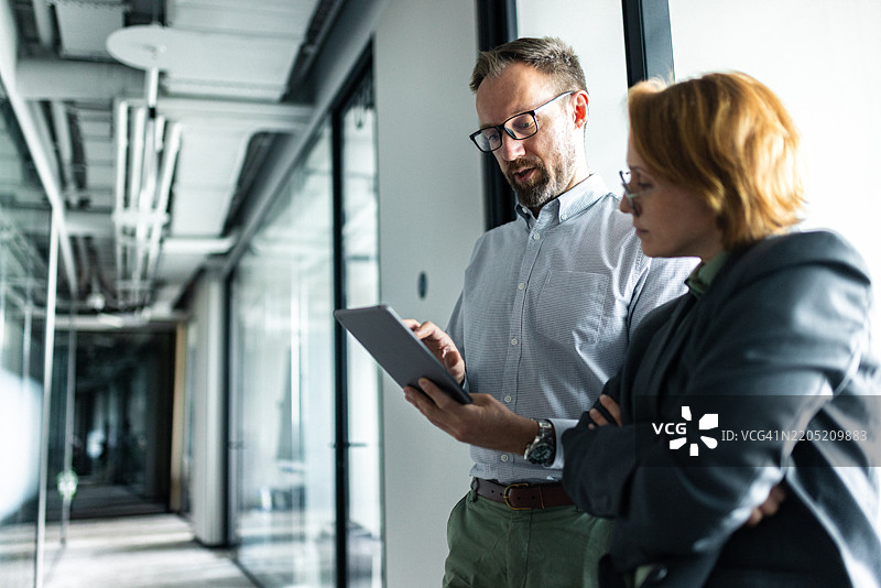 两位专业人士在现代办公室走廊中讨论工作图片素材