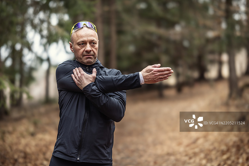 一位五十多岁、外表帅气的运动员在公园里热身，为跑步训练做准备。他正在热身上半身。图片素材