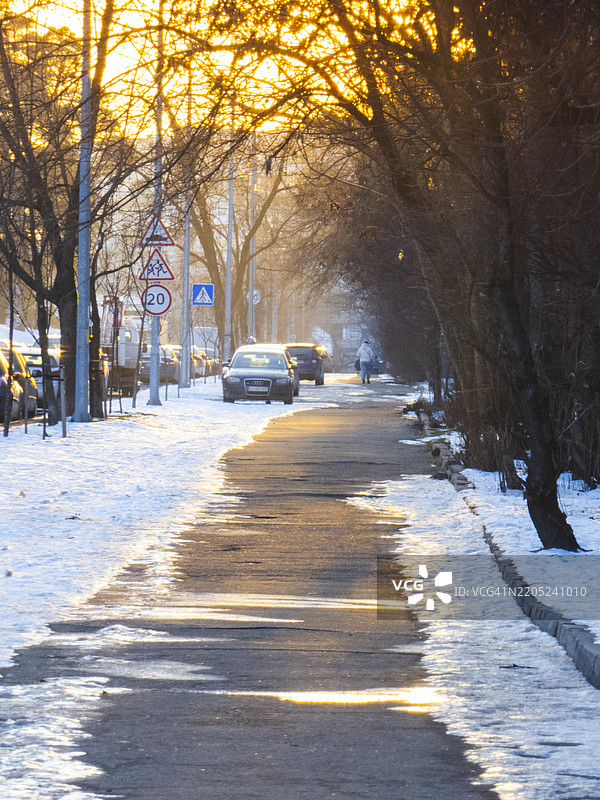 夕阳的余晖照亮了一条宁静的冬季街道，街道两旁是树木和停放的汽车，营造出一个宁静的社区氛围。图片素材