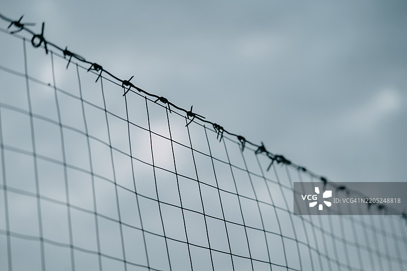 在阴云密布的天空下，链条围栏顶部有刺铁丝。图片素材