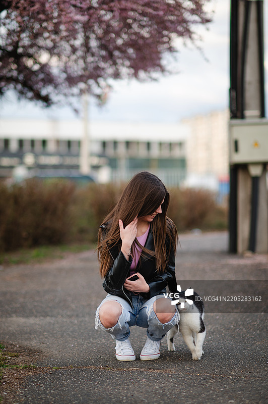 年轻女性蹲下在街上抚摸一只友好的猫咪图片素材