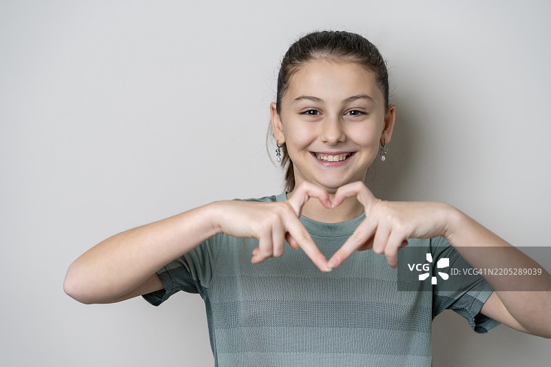 可爱小女孩在白色背景上做心形手势的肖像图片素材