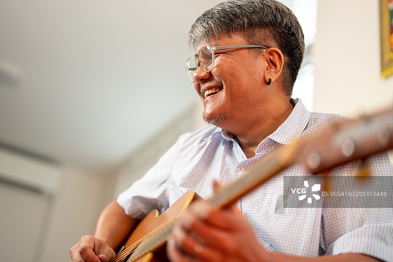 在舒适的室内环境中，微笑着的男人弹奏吉他，展现出对音乐和创意的热情。图片素材