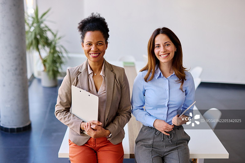 两位微笑的女商人在现代办公室里站着图片素材