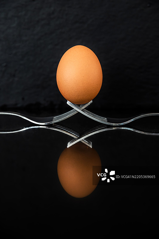 对称特写的鸡蛋放在两把叉子上，背景为黑色图片素材