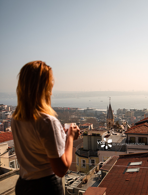年轻女性在伊斯坦布尔城市景观中享受早晨咖啡图片素材