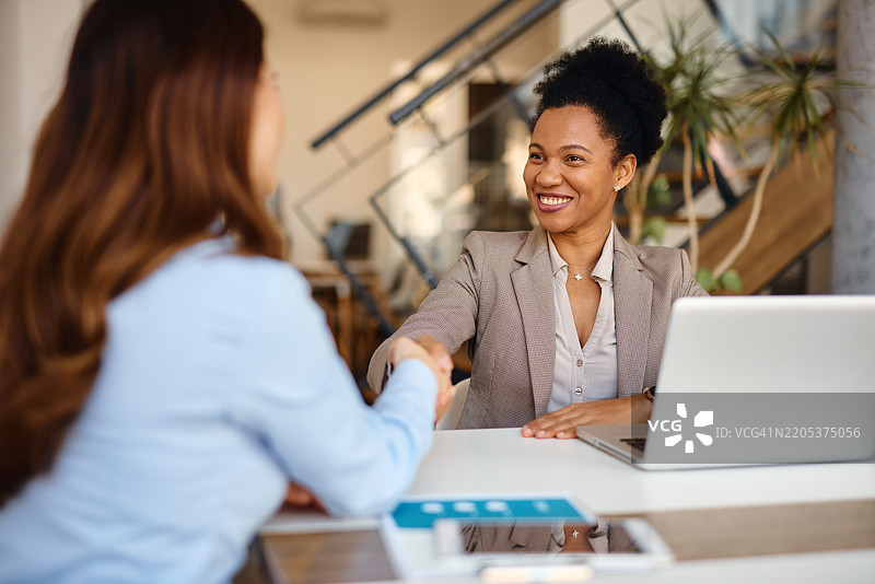 两位女商人在办公室会议期间握手。图片素材