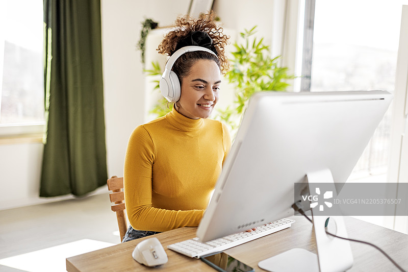快乐的女性在舒适的环境中戴着耳机使用电脑工作图片素材