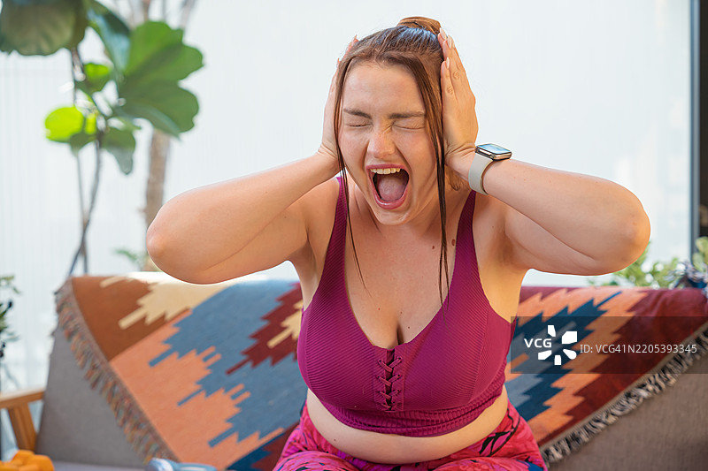 沮丧的胖女人坐在沙发上尖叫。图片素材