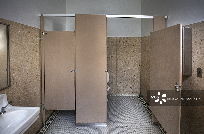 一个空荡荡的废弃建筑中的卫生间隔间，配有马桶和摆动门图片素材