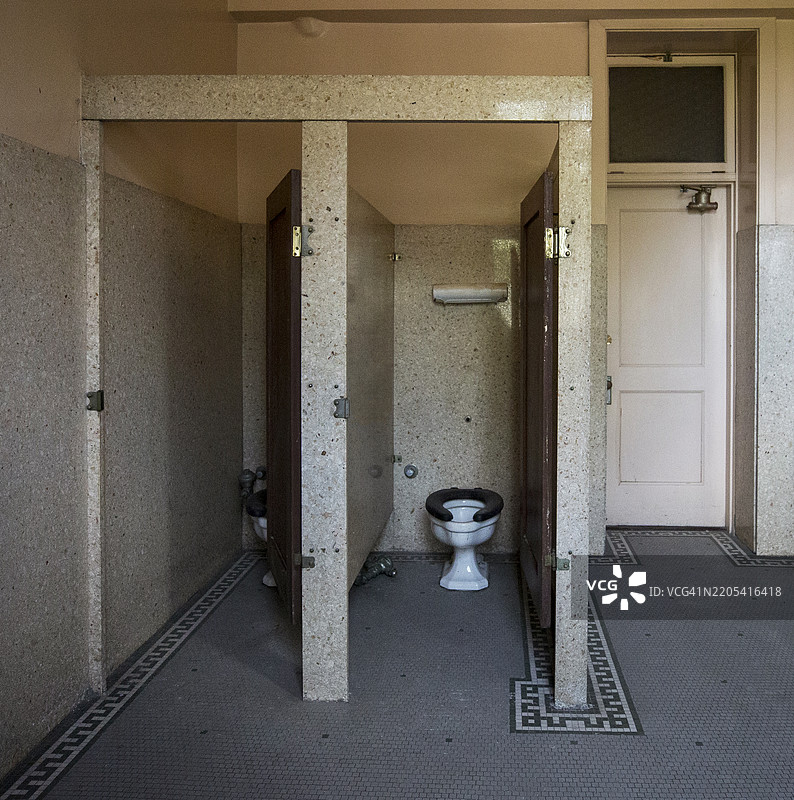 废弃建筑中空荡荡的卫生间隔间，破损的马桶和摇摆的门图片素材