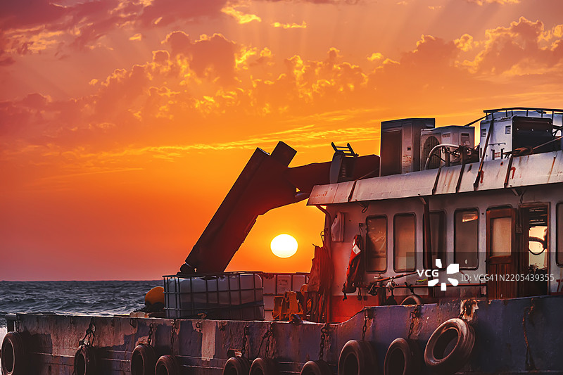 老拖船在风景如画的日落中，夕阳被船上的起重机框住。图片素材