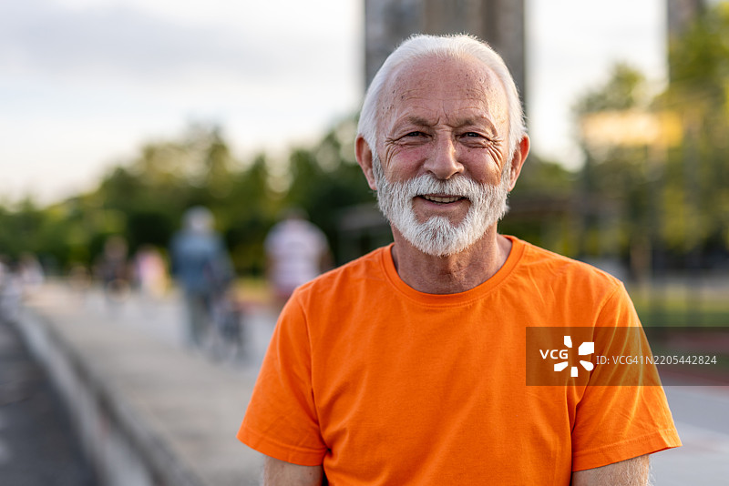 穿着橙色衬衫的微笑老人在公园的肖像图片素材
