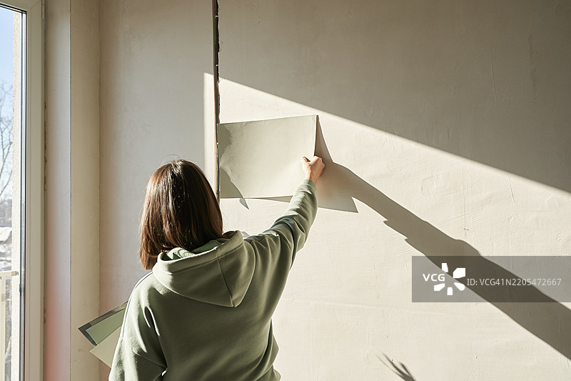 一位女性在纸上用颜料选择墙壁的颜色，并将涂料样本应用到墙上。图片素材