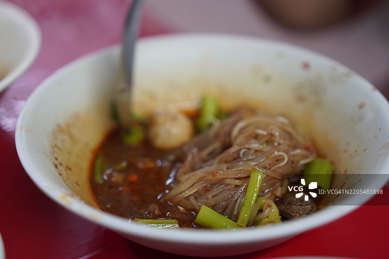 泰式面条，白碗中盛着小面条、炖猪肉、肉丸、猪肝和血汤，搭配木筷和勺子，调味料为食物增添风味，泰国美食美味可口。图片素材