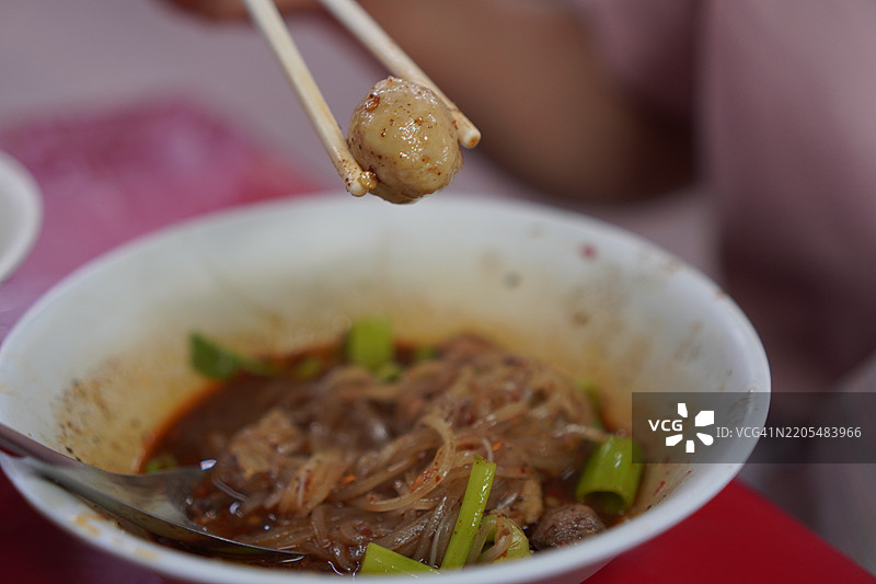 泰式面条，白碗中盛放着小面条、炖猪肉、肉丸、猪肝和血汤，搭配木筷和勺子，调味后美味的泰国菜。图片素材