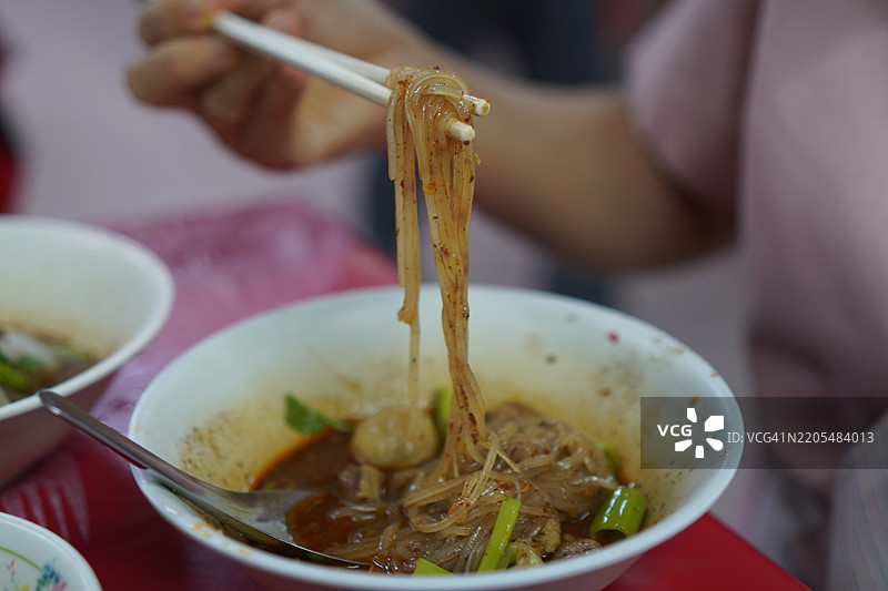 泰式面条，白碗中盛着小面条、炖猪肉、肉丸、猪肝和血汤，搭配木筷和勺子，调味后美味的泰国菜。图片素材