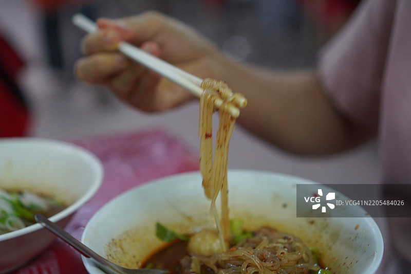 泰式面条，白碗中盛放着小面条、炖猪肉、肉丸、猪肝和血汤，搭配木筷和勺子，调味后美味的泰国菜。图片素材