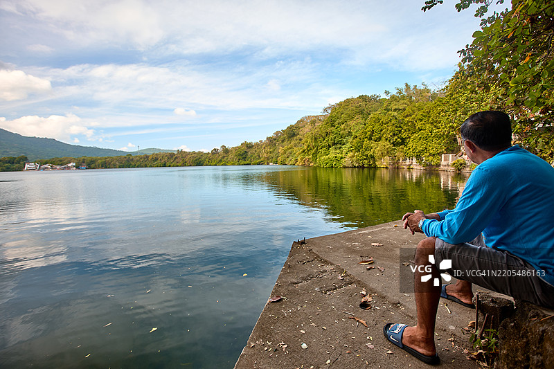 一位渔民坐在拉古纳洛斯巴尼奥斯的鳄鱼湖前，凝视着水面，休息片刻。图片素材