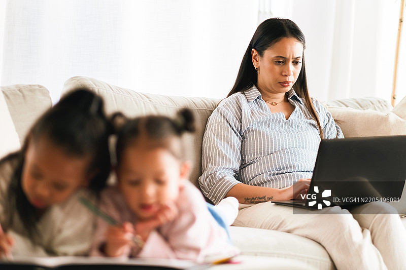 家中，母亲和女性在客厅使用笔记本电脑，认真进行项目，孩子们在旁边打字。远程工作，家庭和父母使用科技进行财务报告，会计和带着孩子的人。图片素材