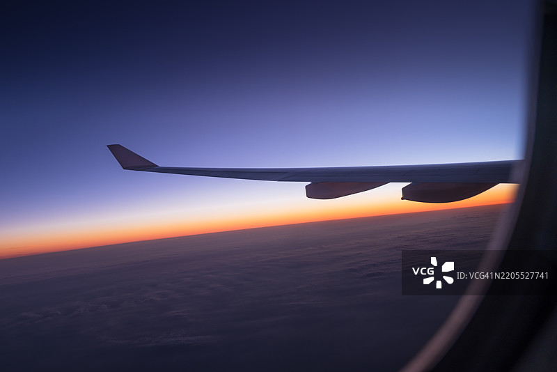 飞机在日落时分飞越云层。图片素材