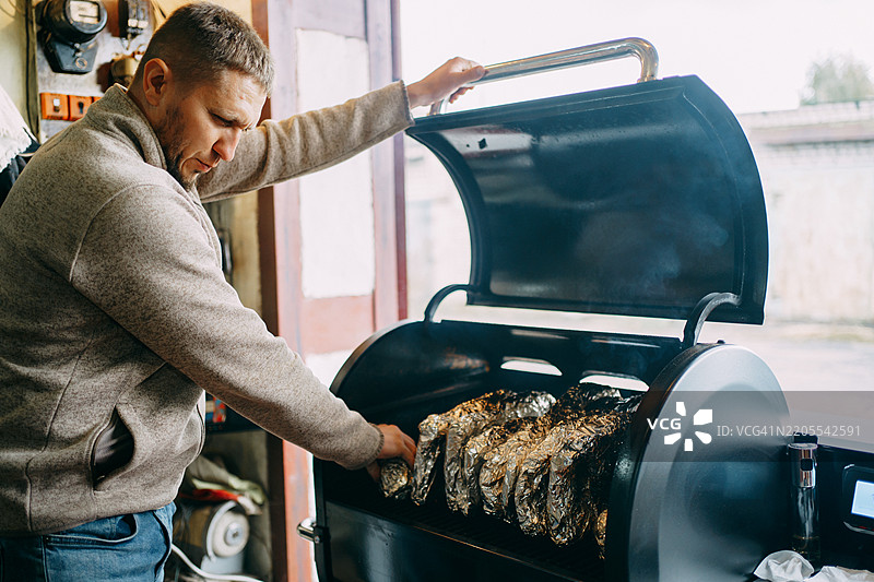 厨师将包裹在锡箔中的食物放入大型烟熏烤架中图片素材