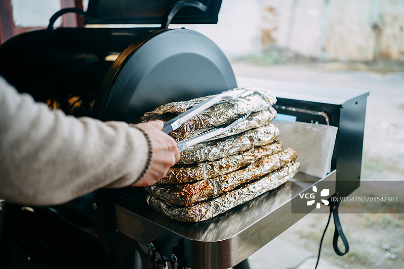 厨师用夹子从烟熏烤架上取出包裹在锡箔中的食物图片素材