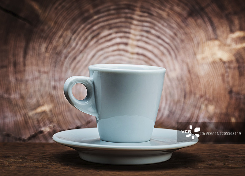 白色陶瓷咖啡杯放在复古木背景上，背景有树干的横截面。图片素材