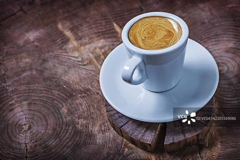 白色咖啡杯里盛着卡布奇诺，放在复古木头横截面树桩上图片素材