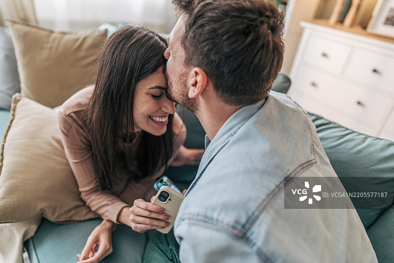 年轻情侣在沙发上放松，分享温馨时刻。图片素材