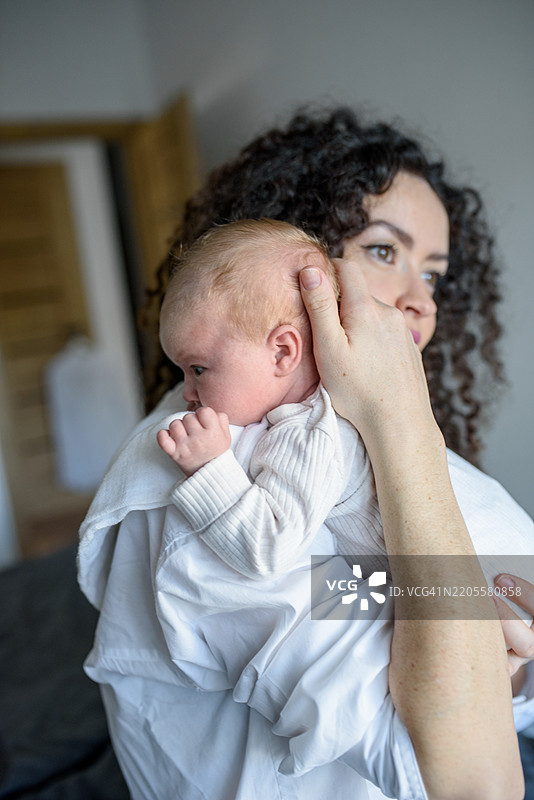 卷发母亲将新生儿抱在肩上。图片素材