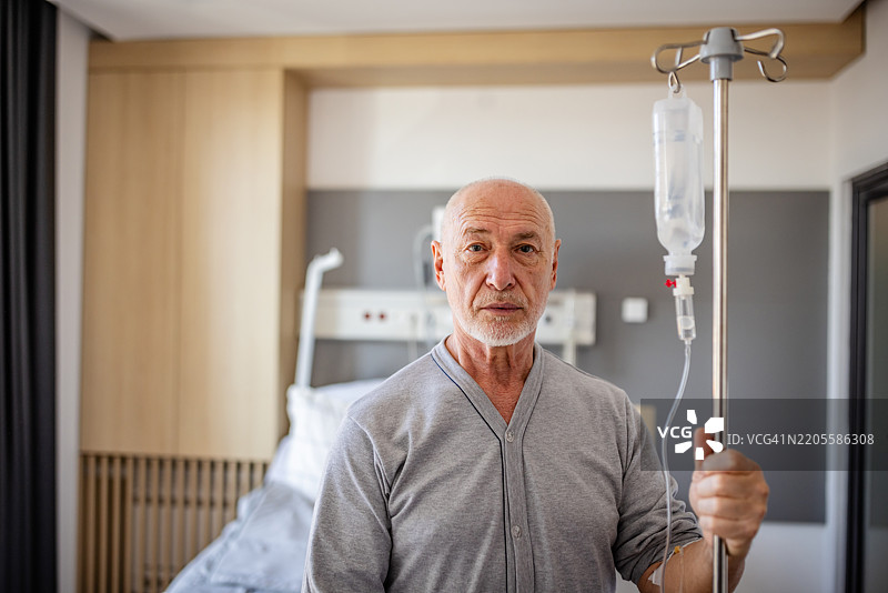 老年男性在医院环境中接受医疗护理，同时握着输液架。图片素材