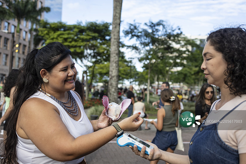 拉丁裔女性在街头派对上使用智能手表通过信用卡付款图片素材