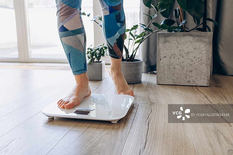 赤脚踩在电子秤上的特写，象征着健康、健身和现代家居环境中的正念。图片素材