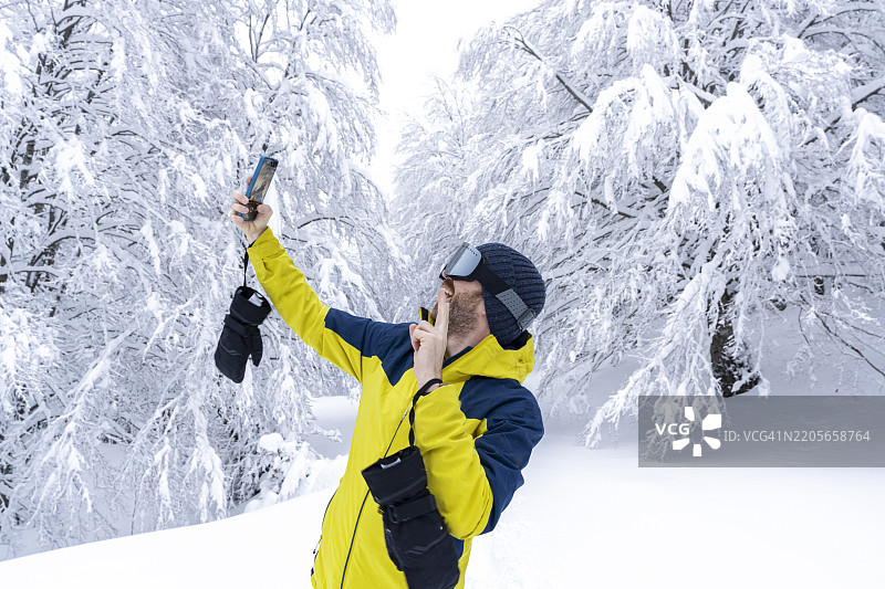 快乐的男人在雪中用智能手机自拍图片素材