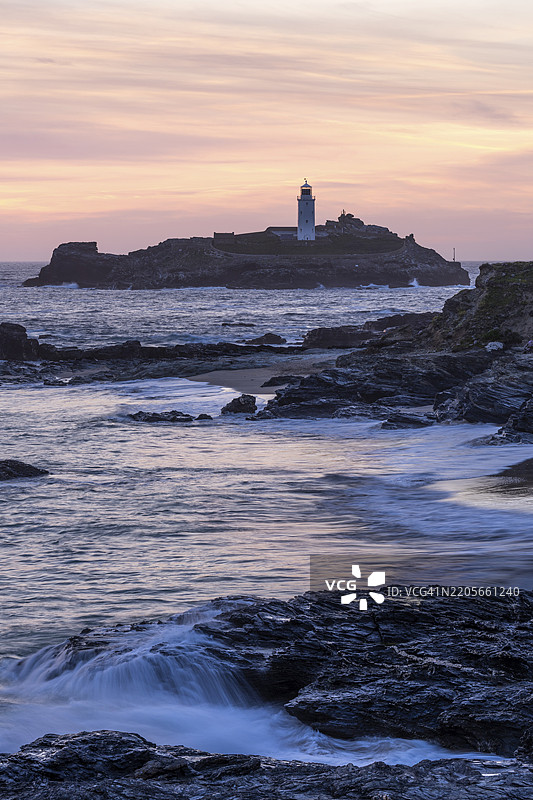戈德里维灯塔，位于戈德里维岛的灯塔，坐落在海中。前景有岩石。黄昏时分，夕阳西下，天空色彩斑斓。英格兰，康沃尔，英国图片素材