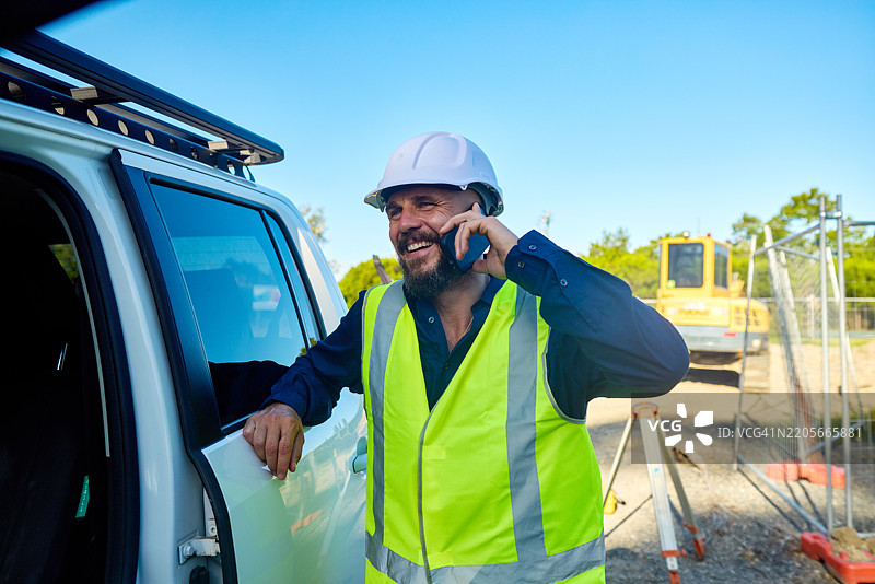 微笑的工程师在澳大利亚的建筑工地上打手机。图片素材