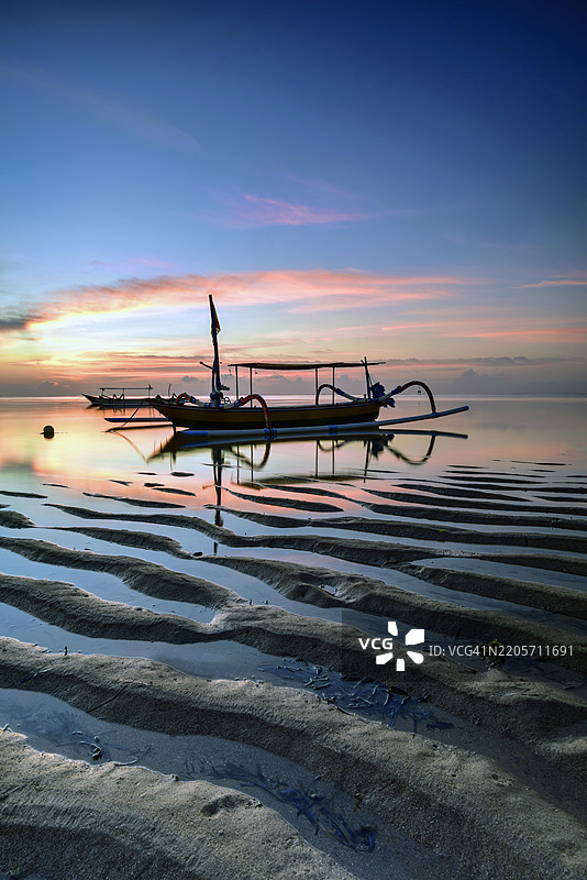 日落时分，传统的朱空船在印度尼西亚巴厘岛沙努尔的梅尔塔萨里海滩停泊的剪影图片素材