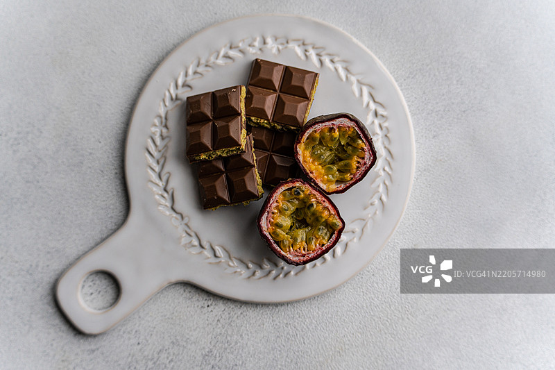 俯视图：一块填充开心果酱的迪拜巧克力棒，旁边放着新鲜的百香果，摆放在一个餐盘上。图片素材